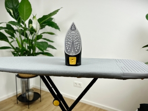 Das Philips Azur 7000 Dampfbügeleisen steht mit seiner Bügelsohle nach oben auf einem grauen Bügelbrett. Die Bügelsohle hat zahlreiche kleine Dampfaustrittslöcher und ist spitz zulaufend.