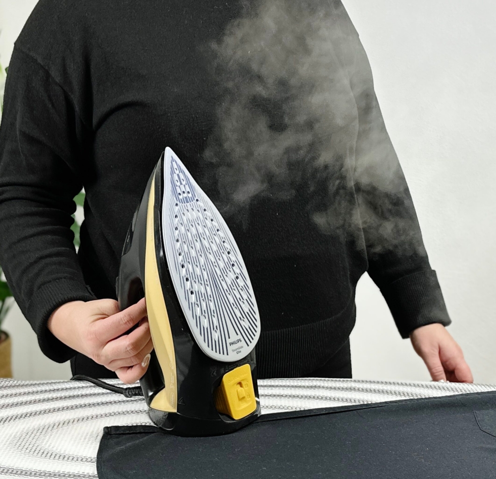 Eine Person in schwarzer Kleidung hält das Philips Azur 7000 Dampfbügeleisen senkrecht auf einem Bügelbrett. Aus der Bügelsohle tritt sichtbarer Dampf aus.