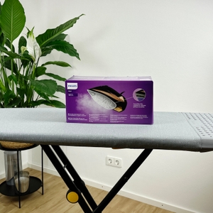 Die Rückseite der Verpackung des Philips Azur 7000 Dampfbügeleisens steht auf einem grauen Bügelbrett. Die Verpackung ist lila mit weißen Texten und zeigt die wichtigsten Funktionen des Bügeleisens.