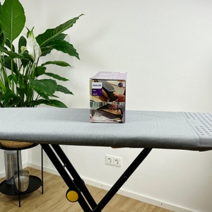 Die Seitenansicht der Verpackung des Philips Azur 7000 Dampfbügeleisens steht auf einem grauen Bügelbrett. Die Verpackung zeigt ein Bild des Bügeleisens sowie Symbole zu seinen Funktionen.