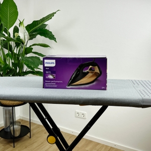 Die Vorderseite der Verpackung des Philips Azur 7000 Dampfbügeleisens steht auf einem grauen Bügelbrett. Das Bild des Bügeleisens ist zentral platziert, daneben befindet sich weißer Text mit Produktinformationen.