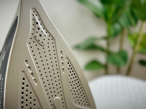 Die Bügelsohle des Rowenta DW6330D1 Eco Intelligence Dampfbügeleisens ist mit mehreren kleinen Dampfaustrittslöchern ausgestattet. Die Oberfläche zeigt leichte Klebereste.