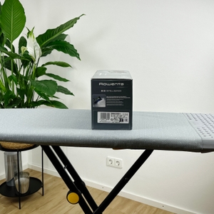 Die linke Seitenansicht der Verpackung des Rowenta DW6330D1 Eco Intelligence Dampfbügeleisens steht auf einem grauen Bügelbrett. Die Verpackung ist schwarz und zeigt weiße Texte sowie grüne Symbole.