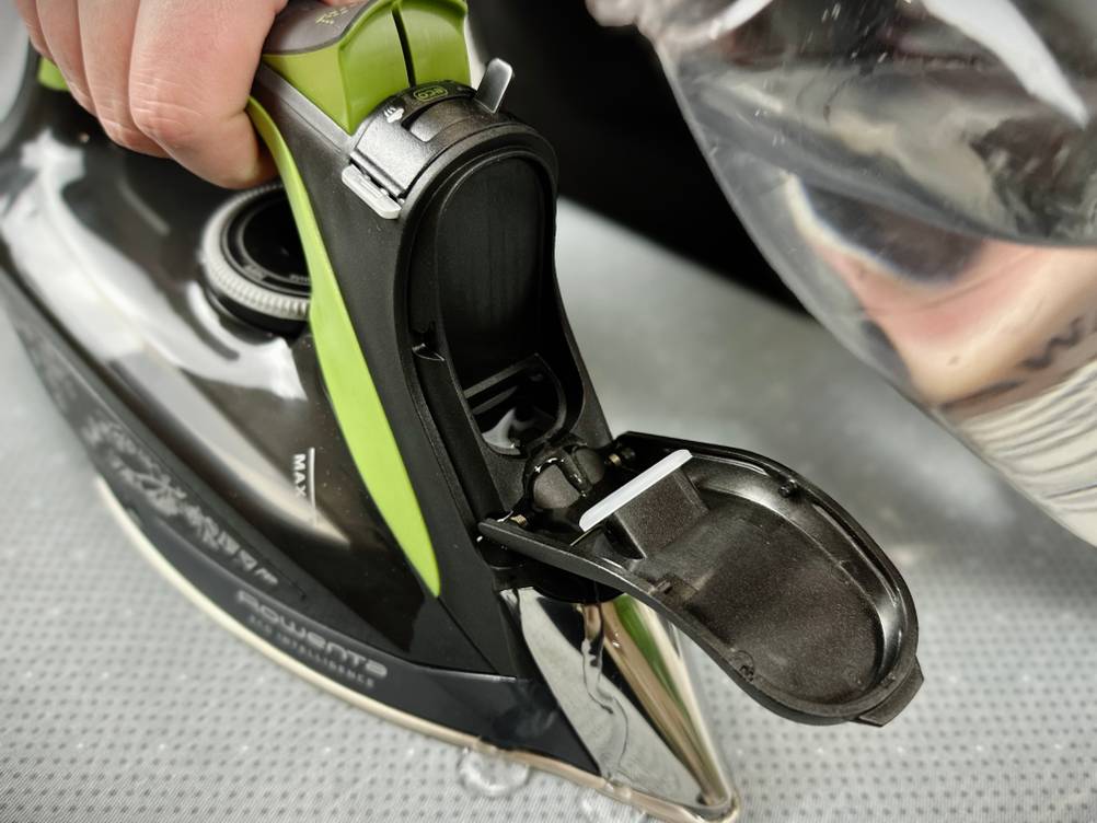 Eine Hand hält das Rowenta DW6330D1 Eco Intelligence Dampfbügeleisen während Wasser aus einem transparenten Gefäß in den geöffneten Wassertank gefüllt wird. Der Einfüllstutzen befindet sich am vorderen Teil des Griffs.