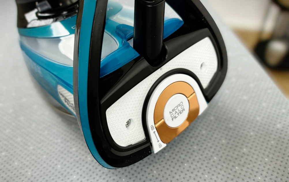 Die Rückseite des Tefal FV9844 Dampfbügeleisens zeigt den runden Micro-Calc-Filter in Bronze und Weiß. Die Filterabdeckung hat ein strukturiertes Design und ist durch Drehen abnehmbar.