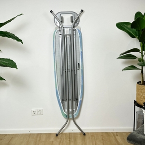 Das Vileda-161484-Bügelbrett steht zusammengeklappt an einer Wand. Die Rückseite zeigt das Metallgestell und die Halterungen.