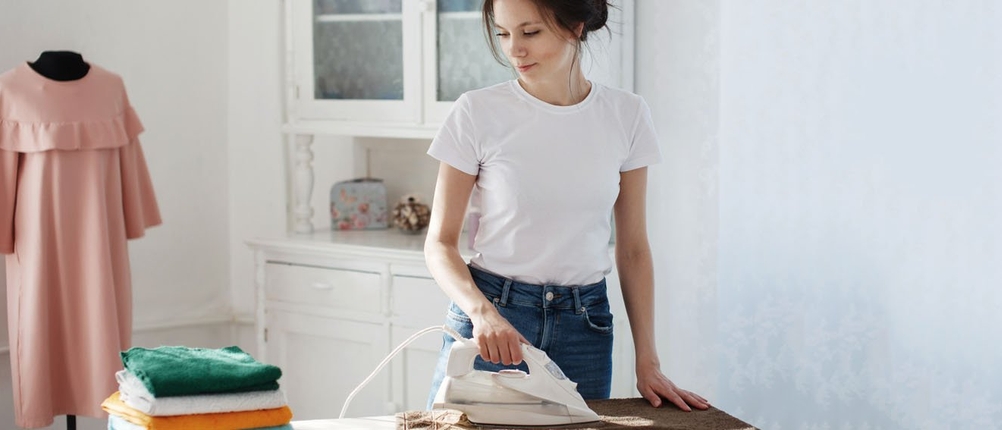 Eine Frau bügelt Kleindung mit einem Bügeleisen.