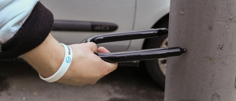 Ein Bügelschloss wird vor eine zu breite Straßenlaterne gehalten.