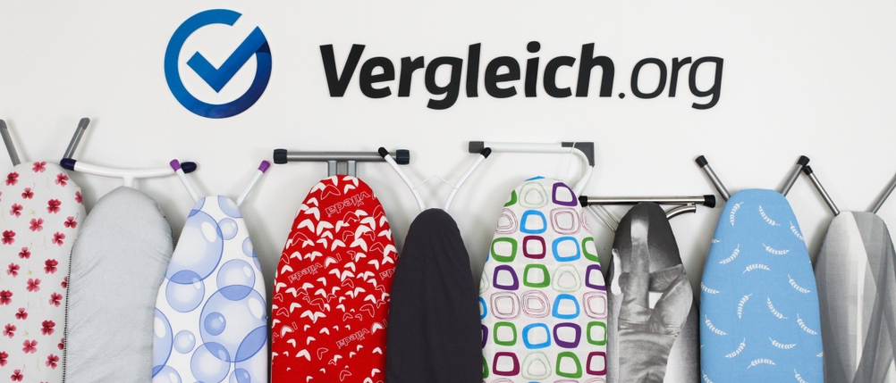 Mehrere Bügelbretter mit unterschiedlichen Bügelbrettbezügen sind an einer weißen Wand angelehnt. 