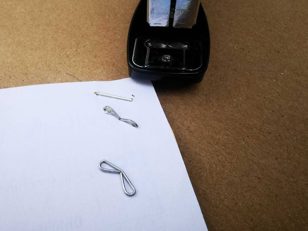 Mehrere Heftklammern liegen getackert in und auf einem Papier, im Hintergrund der getestete Bürotacker.