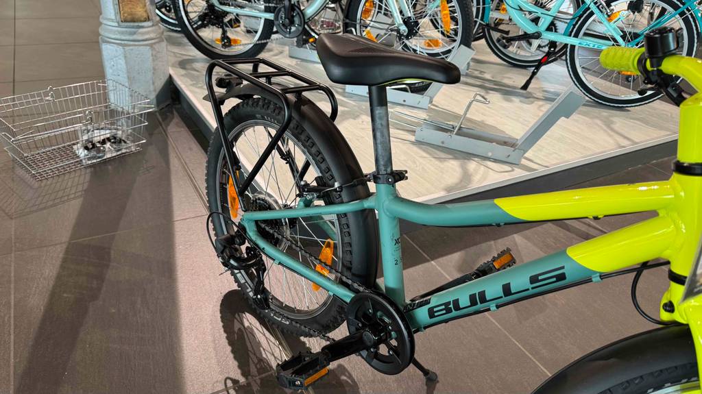 Das getestete 20-Zoll-Fahrrad für Jungs steht mit Fokus auf die Gangschaltung vor einem Ausstellungspodest mit Fahrrädern.