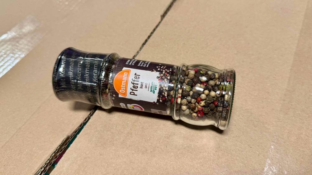 Bunter Pfeffer-Test: Eine transparent verpackte Mühle liegt horizontal auf einem Karton.