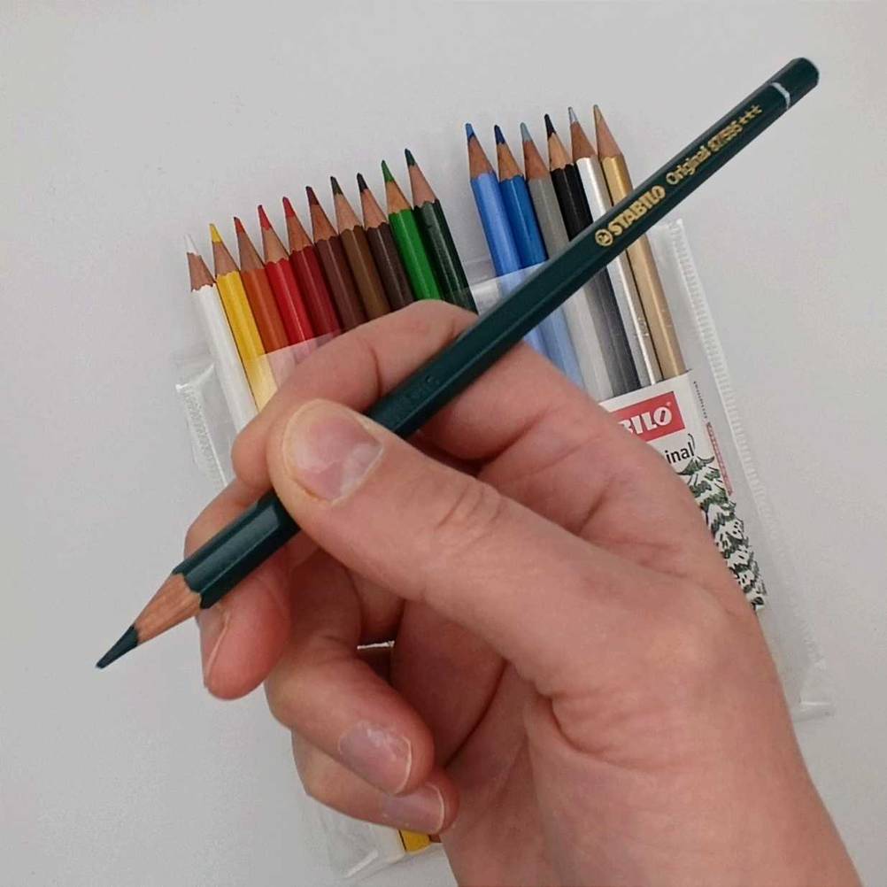 Hand mit Buntstift und im Hintergrund Packung mit Buntstiften.