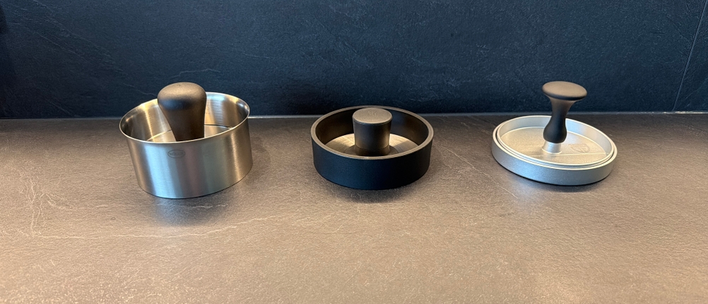 Drei Burgerpressen liegen nebeneinander auf der Arbeitsplatte der Küche