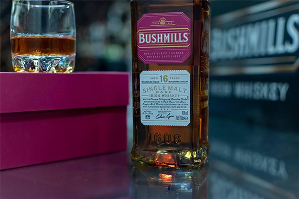 Bushmills-Test: Eine Flasche Bushmills mit 16 Jahren Fassreife auf einem Tisch, daneben ein eingeschenktes Tumbler-Glas.