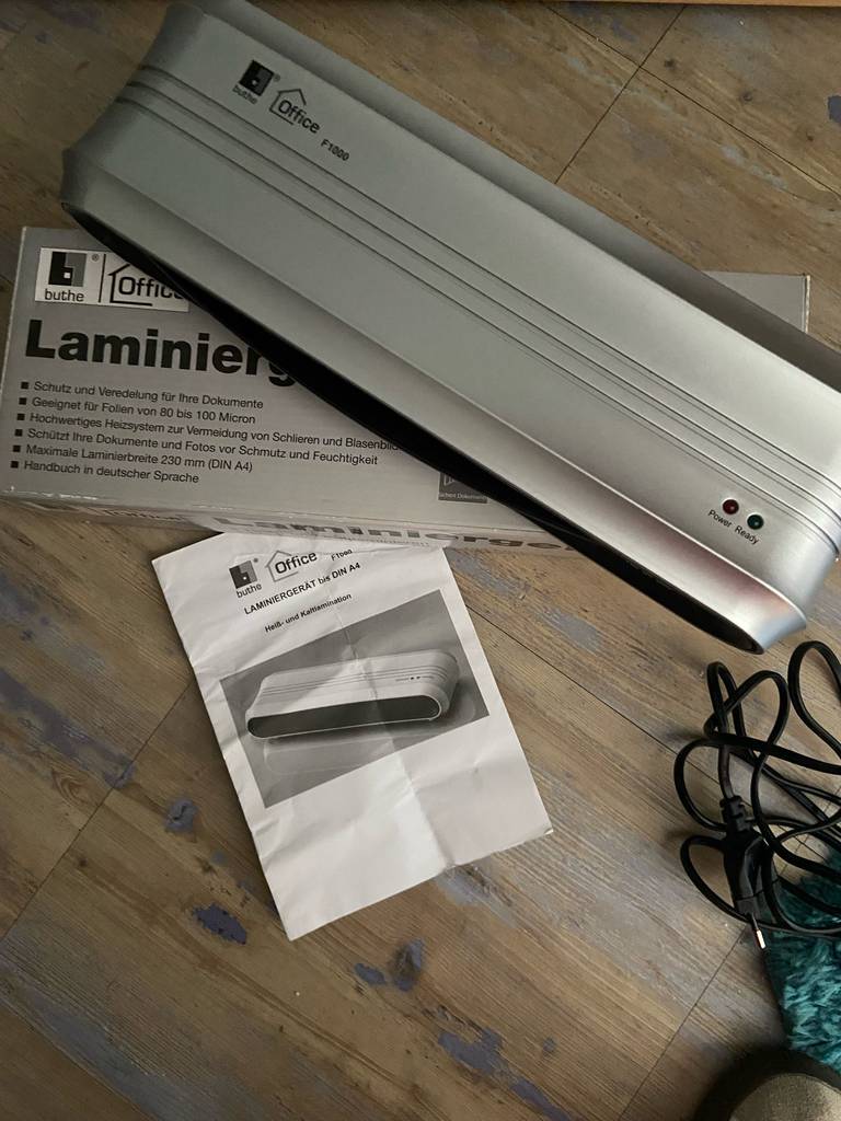 Laminiergerät im Test: Das Modell der Marke buthe befindet sich auf der Verpackung und der Gebrauchsanweisung auf einem Holztisch.