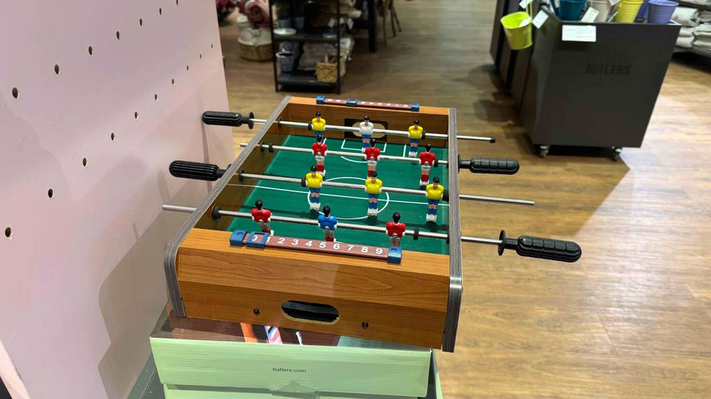 Ein Kinder-Tischkicker im Test steht von der kurzen Seite gesehen auf seinem Karton im Verkaufsbereich.