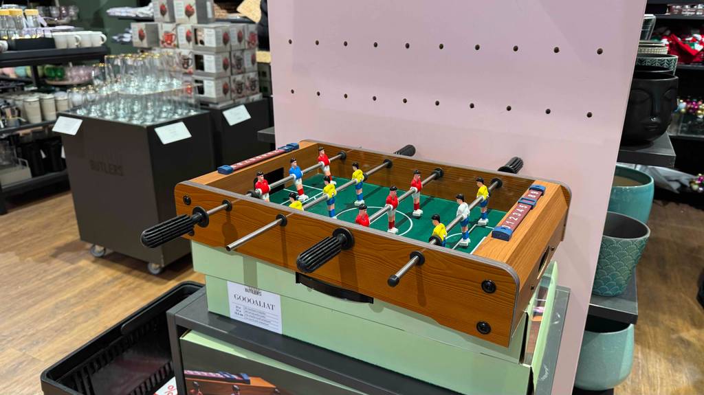 Ein getesteter Kinder-Tischkicker steht von der langen Seite betrachtet auf seinem Karton im Verkaufsbereich.