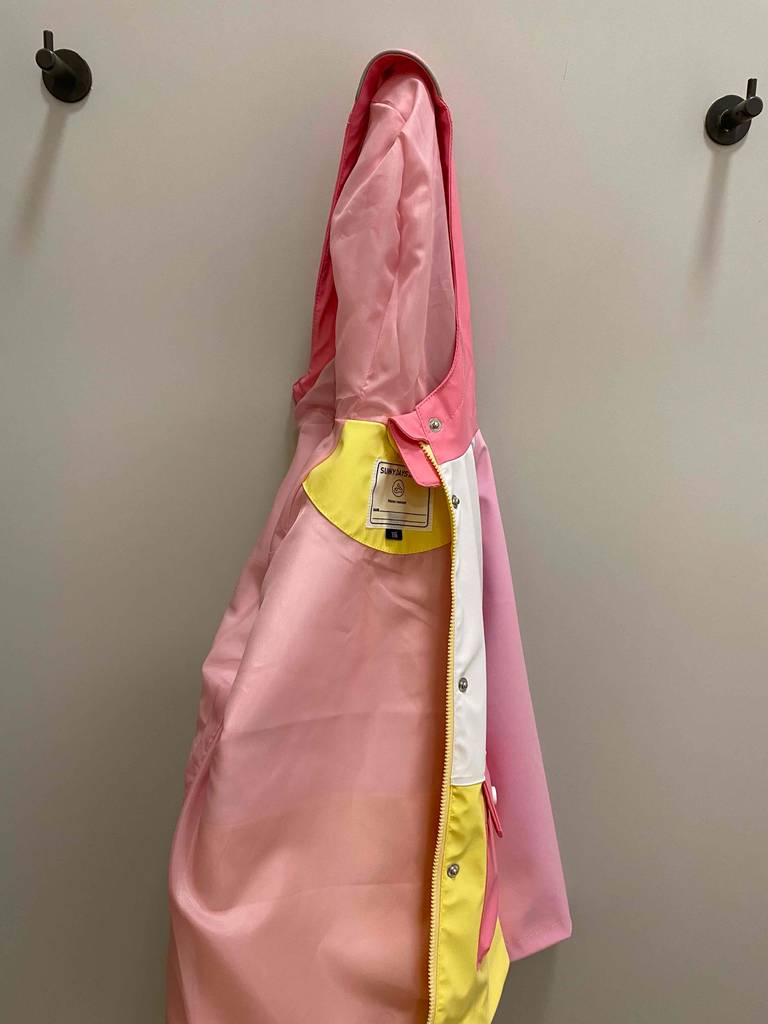 Eine rosafarbene, getestete Regenjacke für Kinder hängt mit Sicht auf das Innenfutter an einem Kleiderhaken.