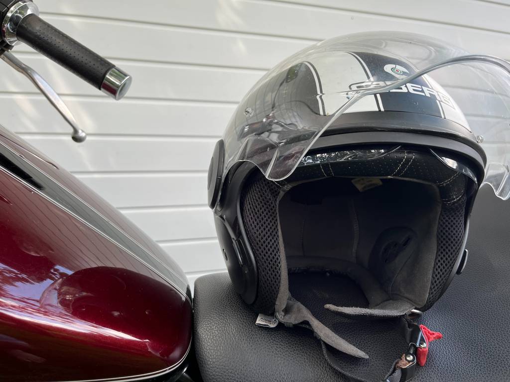 Ein schwarz-weißer Retro Jethelm steht auf dem Sitz eines alten Motorrads in einer Garage.
