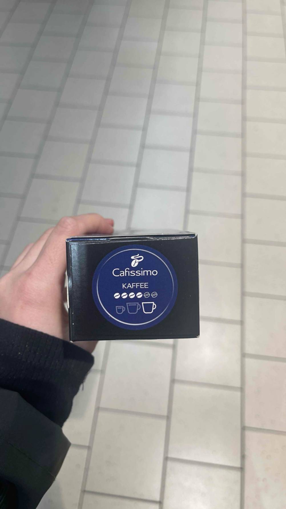 Cafissimo-Kapsel-Test: Eine Hand zeigt den blauen Aufkleber mit vier hervorgehobenen Kaffeebohnen für große Tassen.