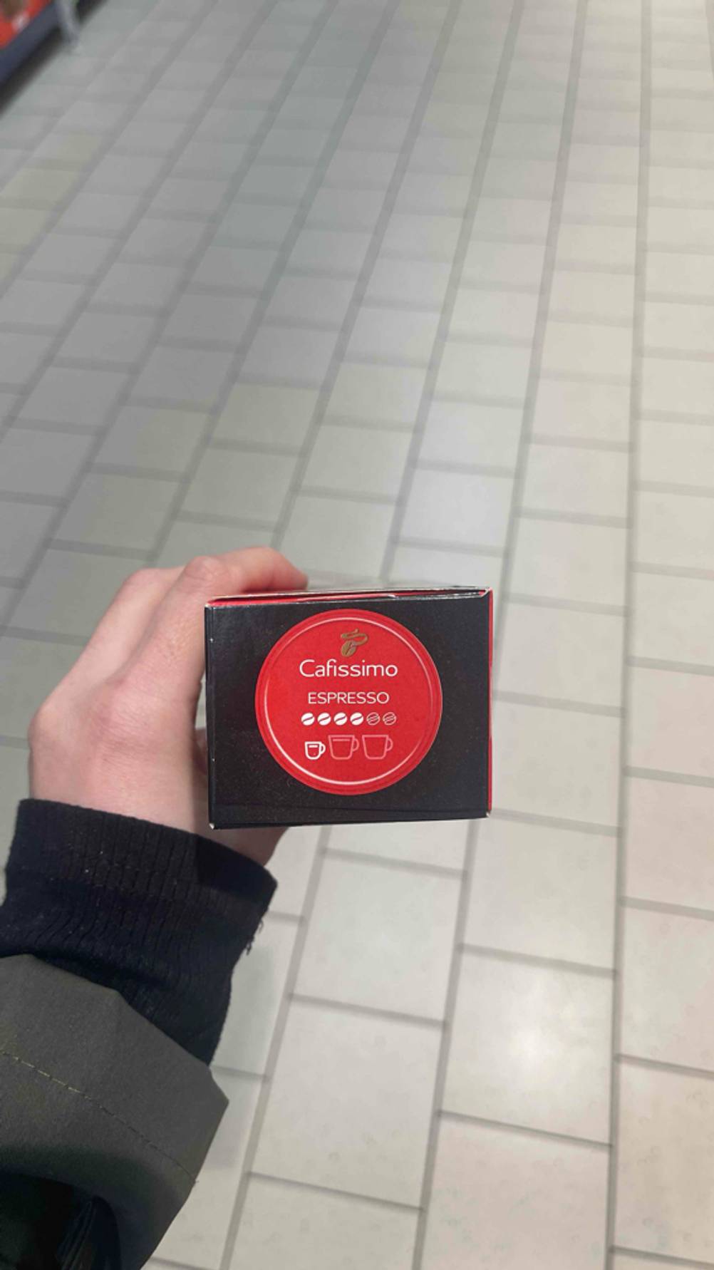 Cafissimo-Kapsel-Test: Eine Hand zeigt den roten Aufkleber mit vier hervorgehobenen Kaffeebohnen für Espresso-Tassen.