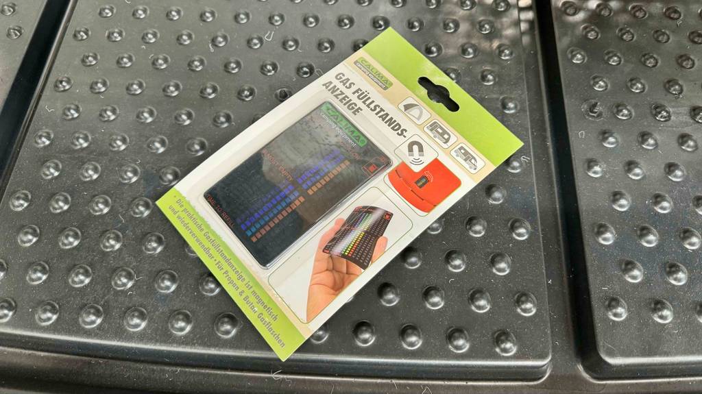 Im Test: Eine Hand zeigt auf der Verpackung die Handhabung eines Gasflaschen-Füllstandsanzeigers.