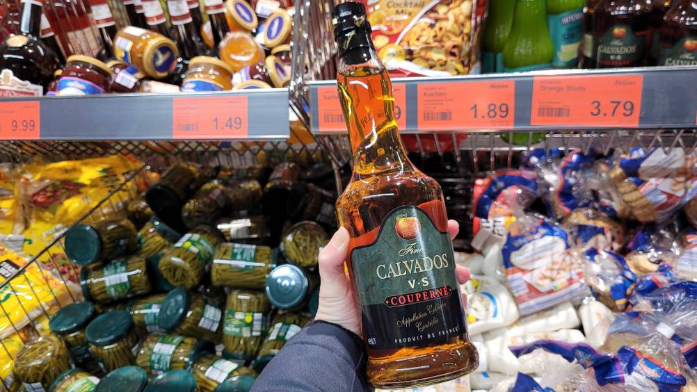 Eine Hand hält den getesteten Calvados vor ein Regal.