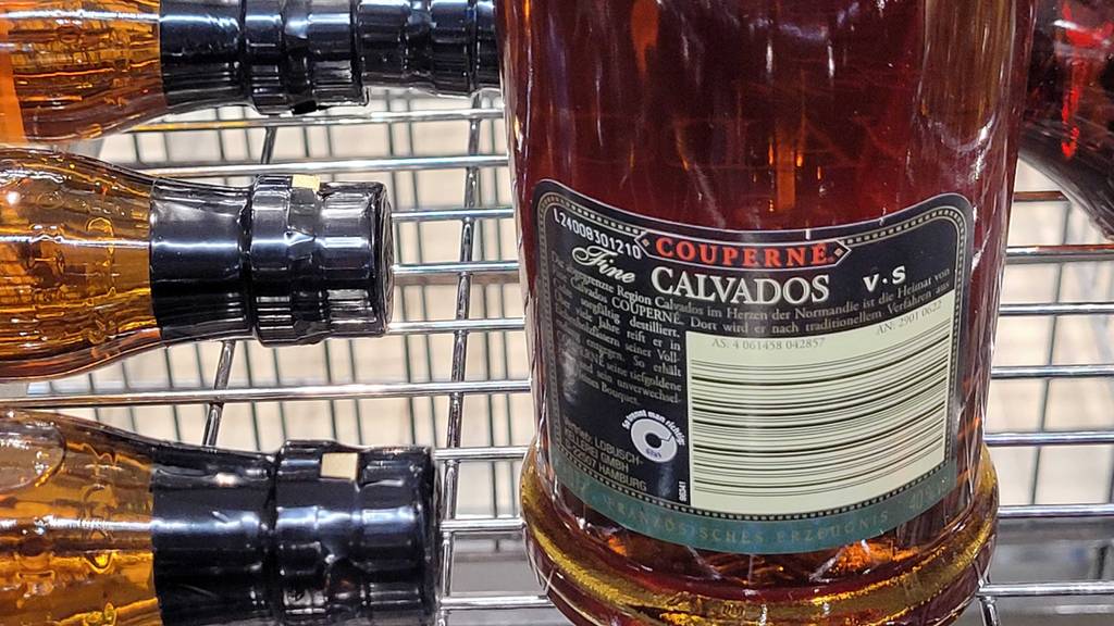 Nahaufnahme des rückwärtigen Produktetiketts einer transparenten Glasflasche mit goldbraunem Calvados Brandys im Test in einem Verkaufsregal.
