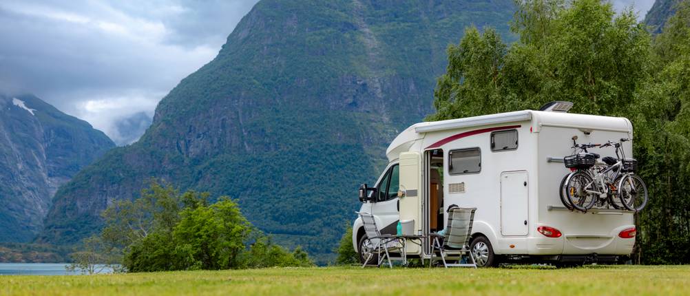 Wohnmobil mieten getestet: Auf einer Wiese steht ein Wohnmobil. Im Hintergrund vernebeln Wolken die Spitze eines Berges.