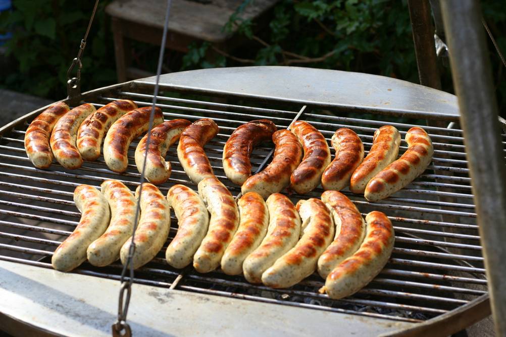 Bratwürstchen werden auf einem Schwenkgrill gegrillt.