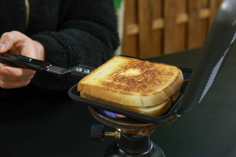 Camping-Toaster-Test: Camping-Toaster-Pfanne über Gasbrenner mit Toastbrot.