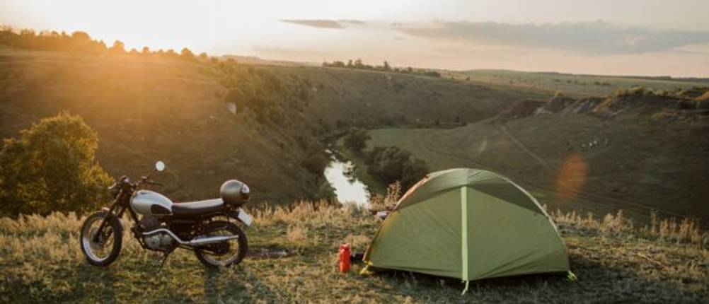 Camping und Motorradfahren im Test: Aufgebautes Zelt neben geparktem Motorrad vor einem Sonnenuntergang.