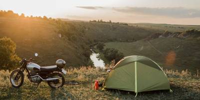 Camping und Motorradfahren im Test: Aufgebautes Zelt neben geparktem Motorrad vor einem Sonnenuntergang.