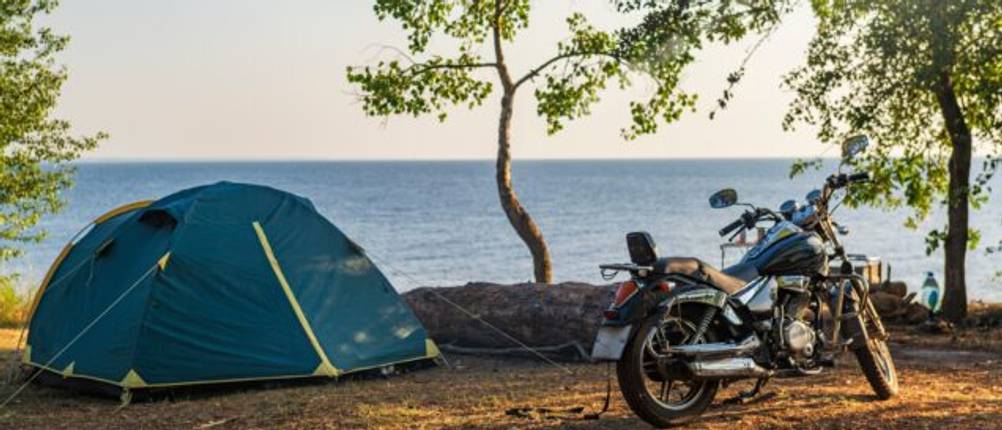 Motorradfahren beim Camping getestet: Motorrad steht neben einem Zelt an der Küste vor einem Ozean.