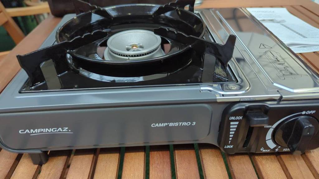 Gaskocher im Test: Der graue Standkocher Camp Bistro 3 von Campingaz von schräg oben mit einem Brenner und Regler auf Holz.