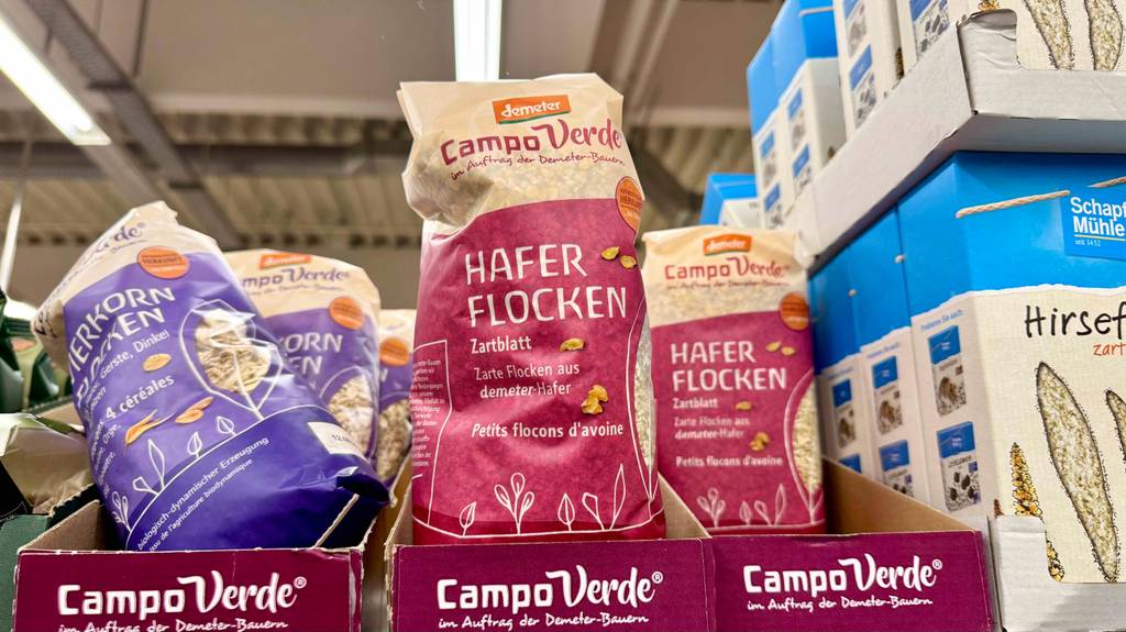 Mehrere Packungen der Marke Campo Verde mit getesteten zarten Haferflocken stehen in einem Karton auf dem Supermarktregal neben Haferflocken anderer Marken.