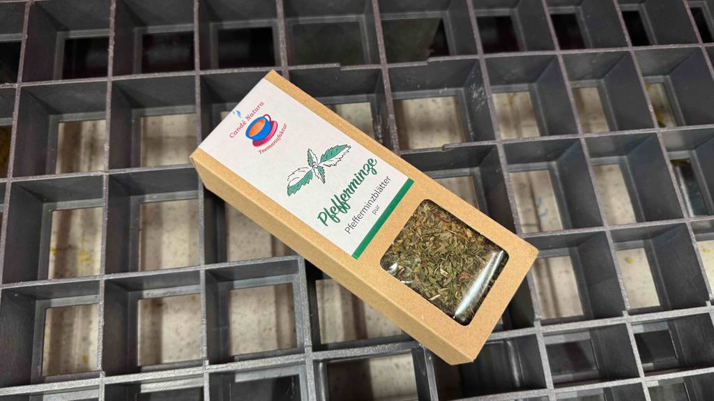 Eine Schachtel mit getestetem Pfefferminztee liegt auf einem Gitter.
