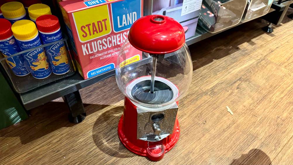 Ein getesteter Candy-Grabber von schräg oben auf einem Holzboden vor einem Verkaufsregal.
