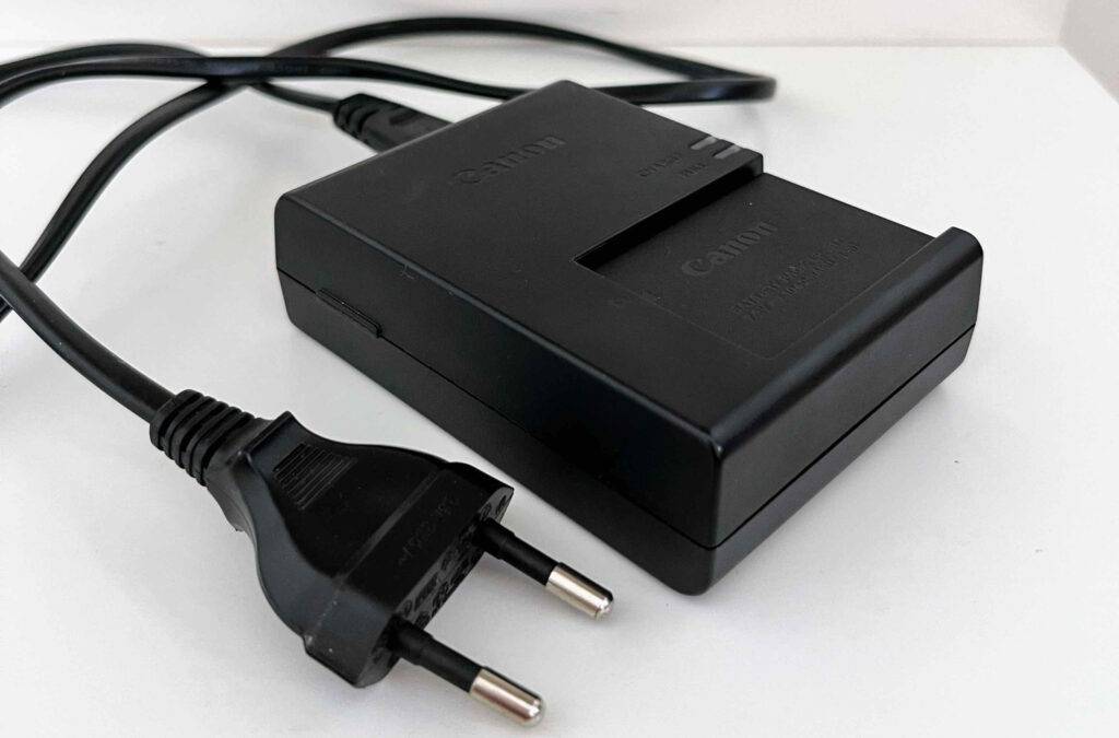 Akku-Ladegeräte im Test: ein schwarzes Canon Modell inklusive Ladekabel liegt auf einer weißen Oberfläche.