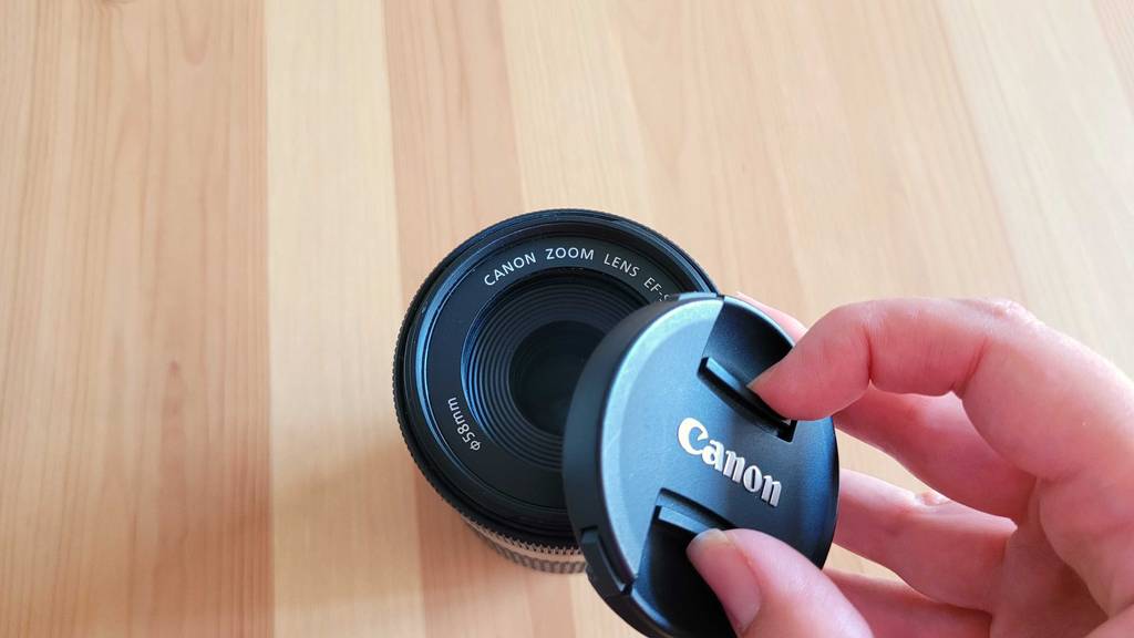 Teleobjektiv im Test: Hand nimmt Deckel eines Canon Objektivs ab.