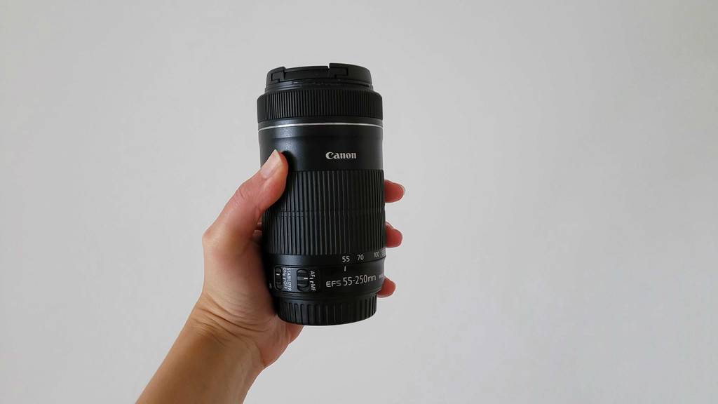 Teleobjektiv im Test: Hand hält ein Canon Objektiv vor weißer Wand.