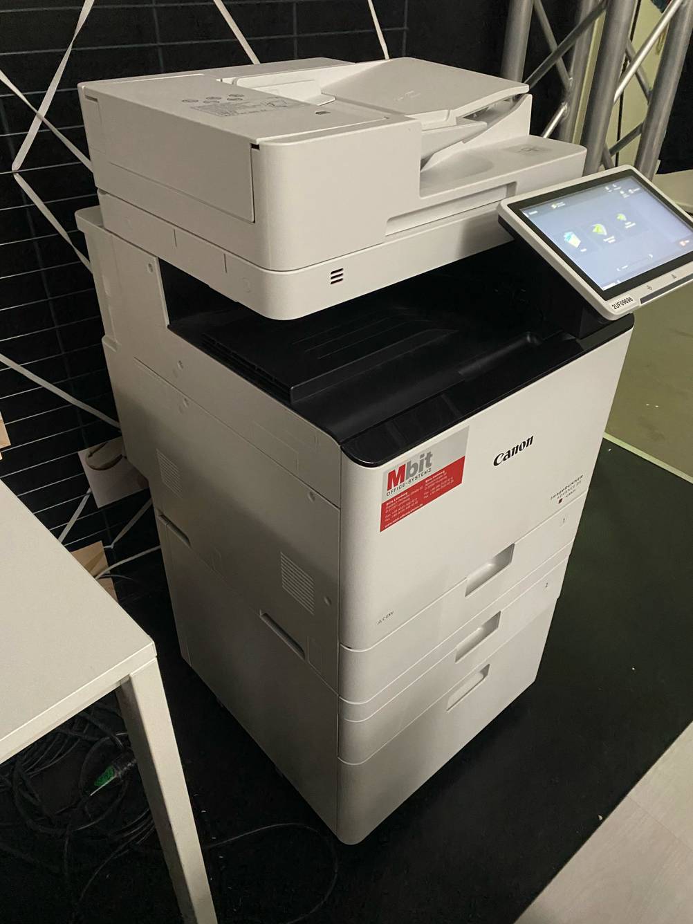 Ein getesteter Laserdrucker-WLAN von schräg vorne auf einer dunklen Fläche stehend.