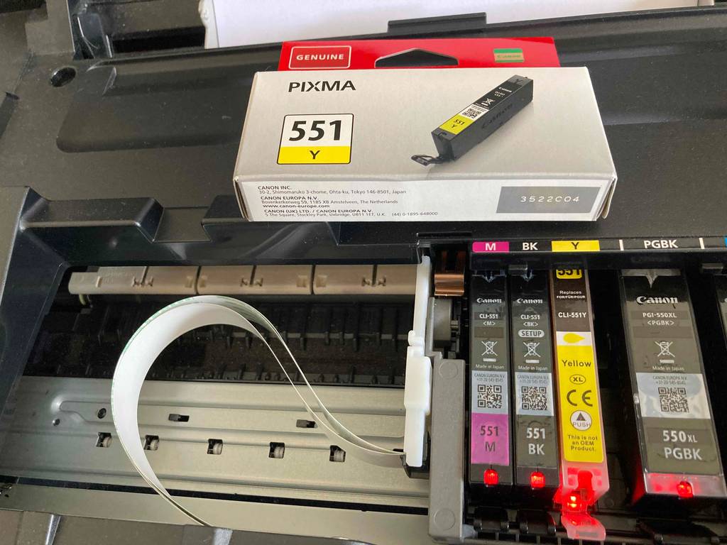 Eine austauschbare Farbpatrone liegt in einer Originalverpackung auf einem geöffneten A3-Drucker im Test, mit Fokus auf die vorhandenen Farbpatronen.