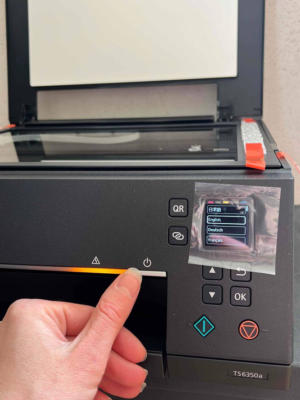 Ein Drucker, der geöffnet ist und eine Hand auf dem On-Knopf liegend.