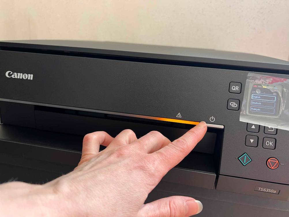 Ein schwarzer Drucker, bei dem eine Hand auf den On-Knopf zeigt.