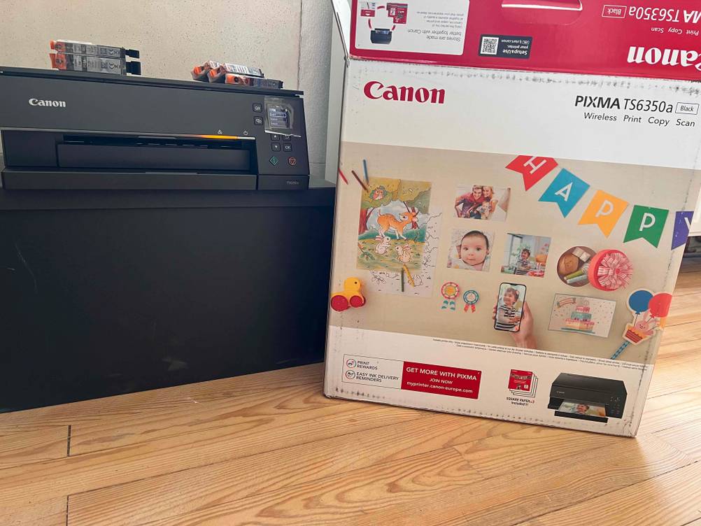 Ein getesteter Canon PIXMA neben seiner Originalverpackung auf einem dunklen Regal.