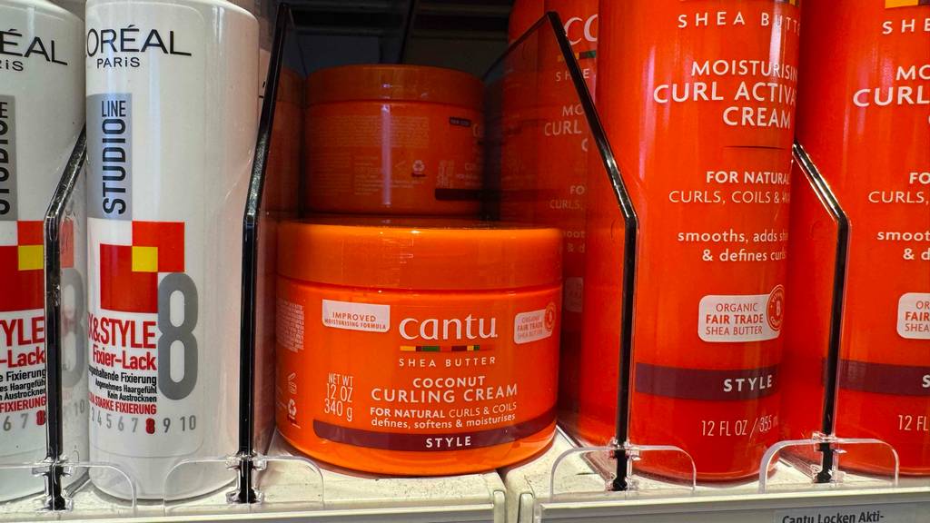 Lockencreme im Test: Mehrere Dosen stehen hinter- und aufeinander in einem Regal zwischen anderen Pflegeprodukten.