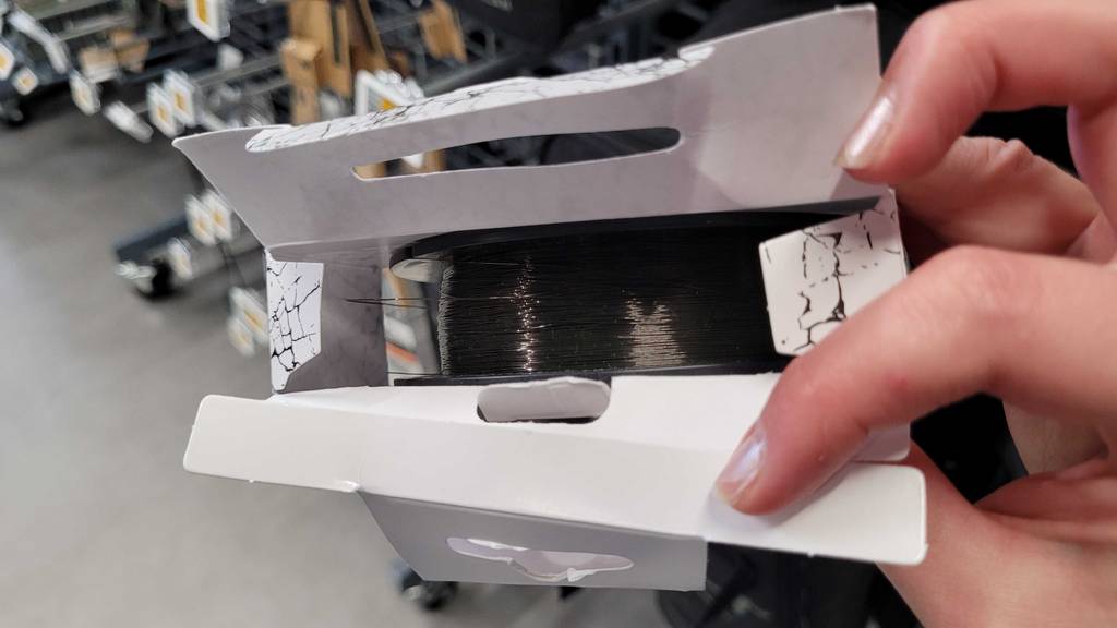 Im Test: Eine Hand öffnet eine Packung mit inliegender Karpfenschnur.