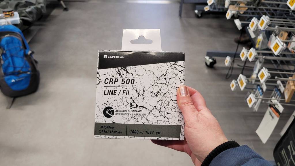 Im Test: Eine Hand hält eine Packung Karpfenschnur über einem Betonboden.
